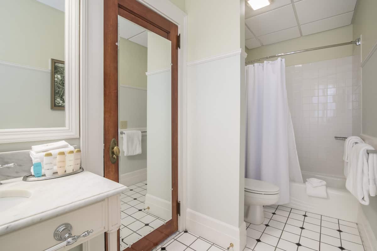 A bathroom with a white sink, mirror, and toilet. There are toiletries on the sink, and a shower curtain is visible.