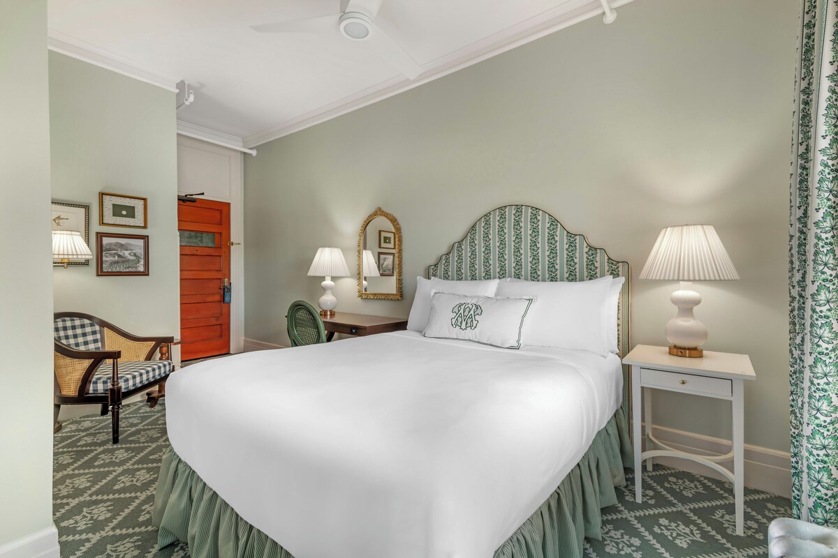 Une chambre d’hôtel avec un grand lit, un bureau, une chaise, une table de chevet et une porte.