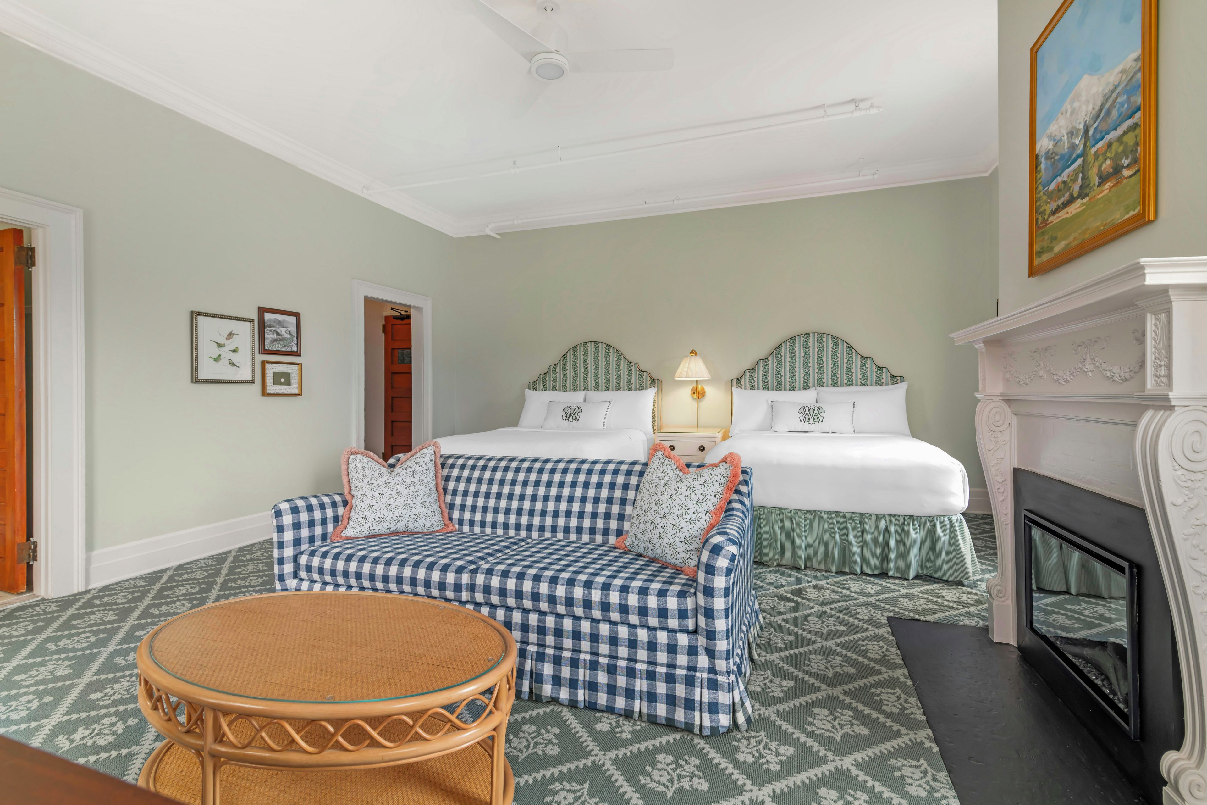 A hotel room with a checkered sofa, a round table, a bed with a headboard, a fireplace, and a painting on the wall.