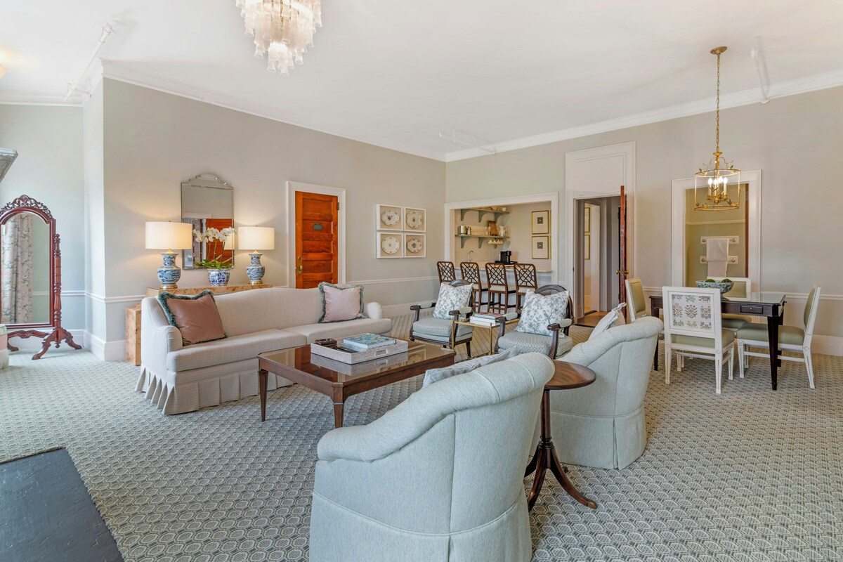 Een ruime woonkamer met een bank, fauteuils, een salontafel en een eethoek met stoelen en een tafel.