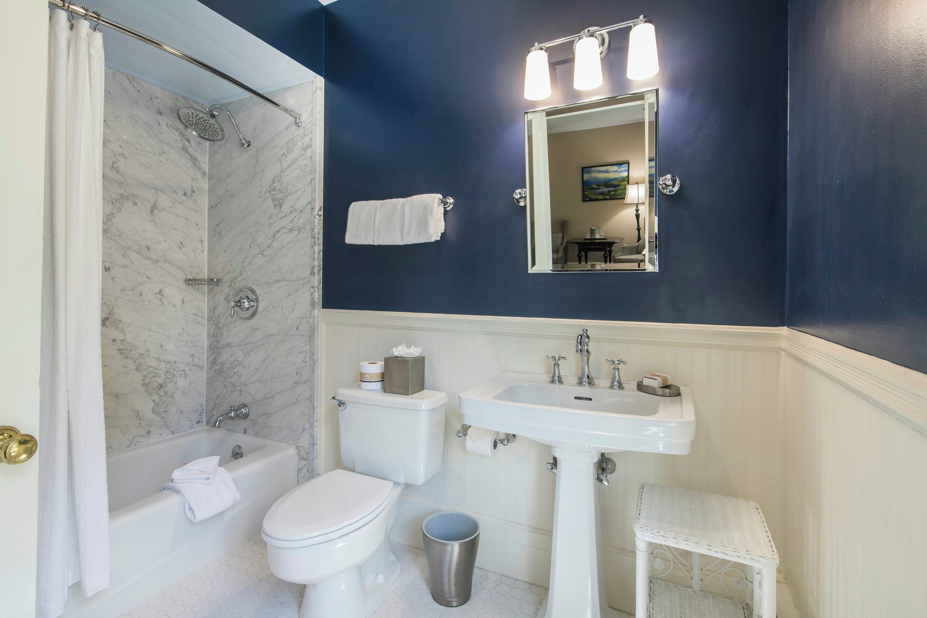 A bathroom with a shower, toilet, sink, and a small step stool.