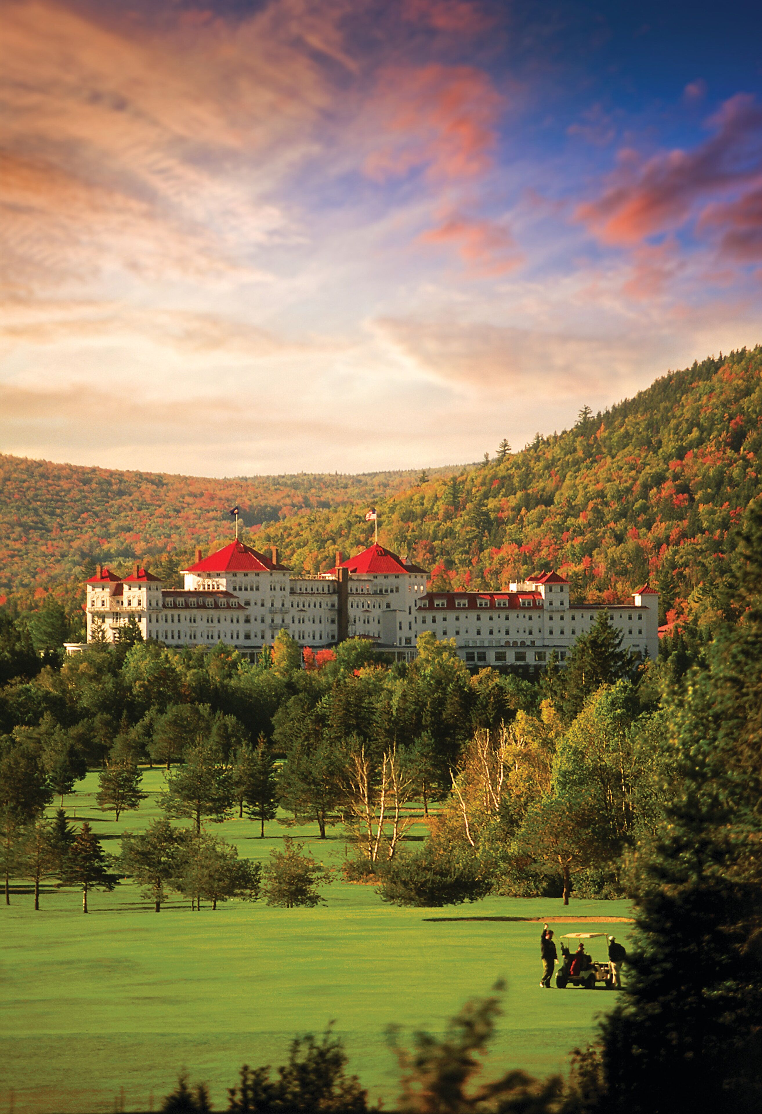 A large, multi-story building with red roofs, surrounded by a lush green landscape and trees.