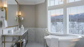 Un baño moderno con una bañera independiente, un tocador con marco dorado y un espejo grande.