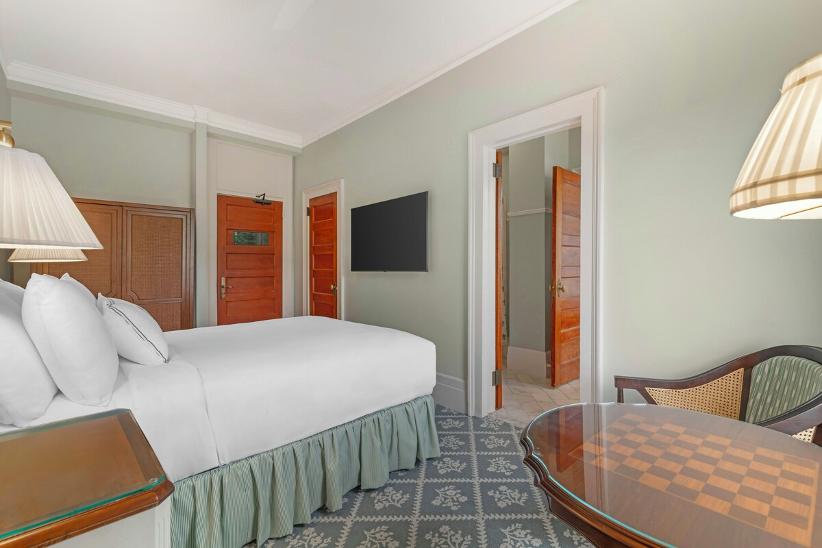 Une chambre d’hôtel comprenant un lit, un bureau avec une chaise, une télévision et une porte donnant sur une autre pièce.