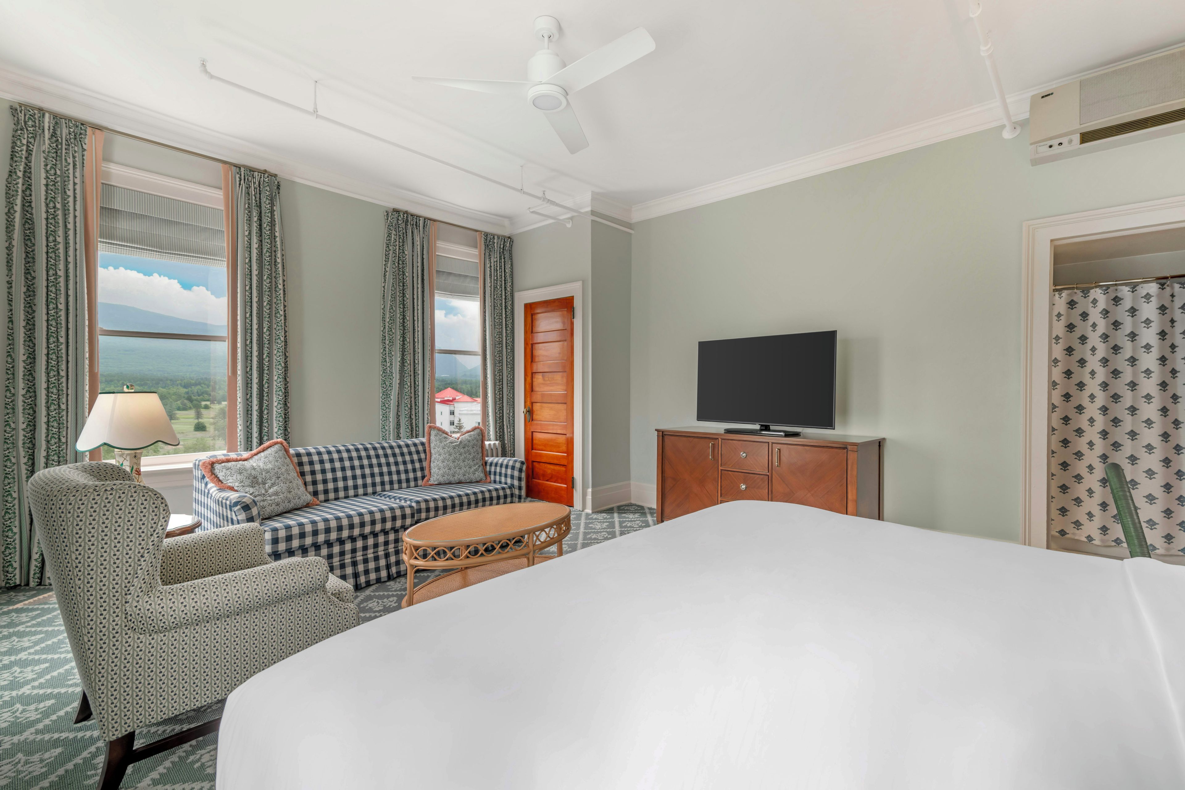 A hotel room with a bed, a sofa, a television, and a window with curtains.