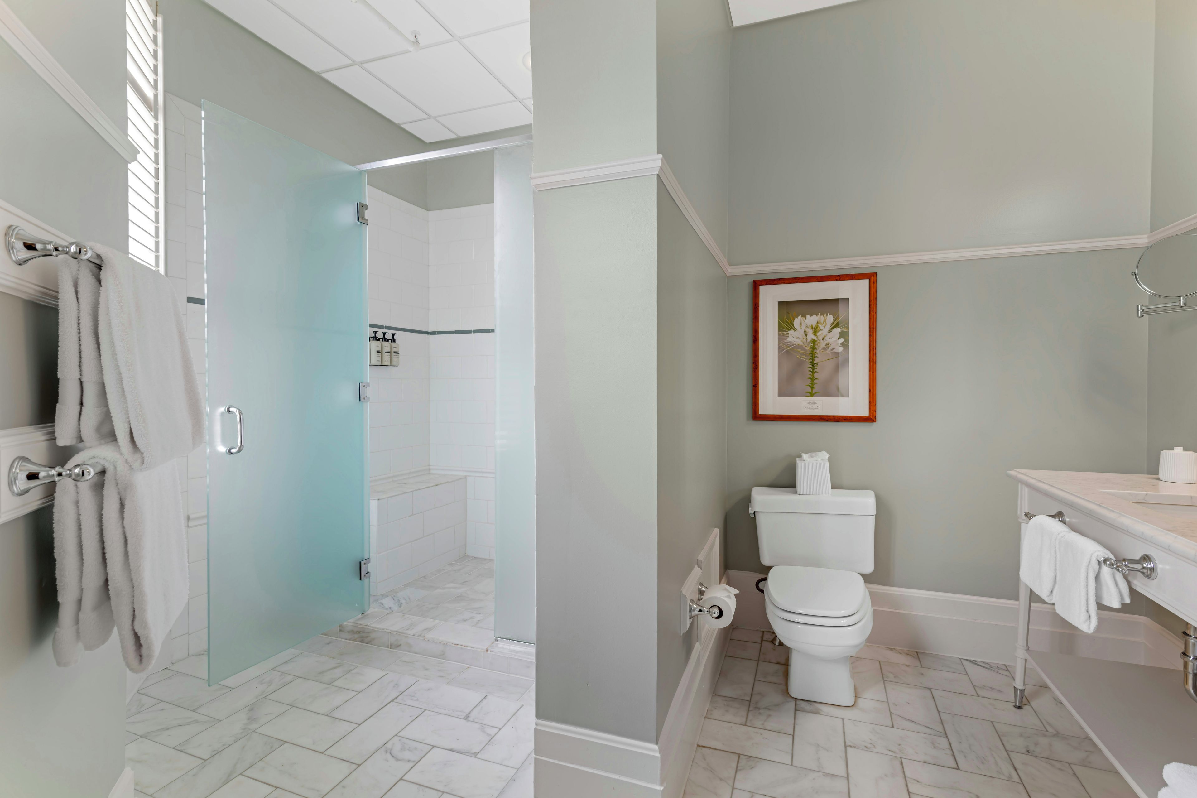 Een badkamer met een glazen douchedeur, witte tegels, een toilet en een wastafel met spiegel.