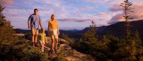 Eine vierköpfige Familie auf einem felsigen Bergpfad mit herrlicher Aussicht auf Berge und Himmel.