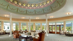 A grand lobby with a high ceiling, large windows, and a central seating area with sofas and armchairs.