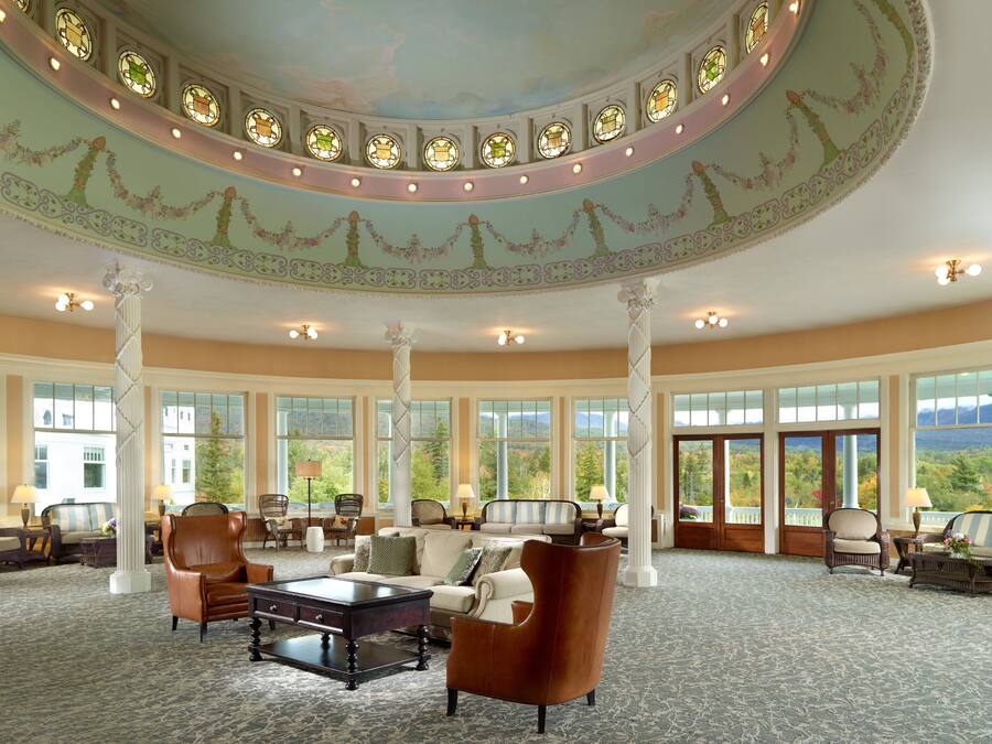 A grand lobby with a high ceiling, large windows, and a central seating area with sofas and armchairs.