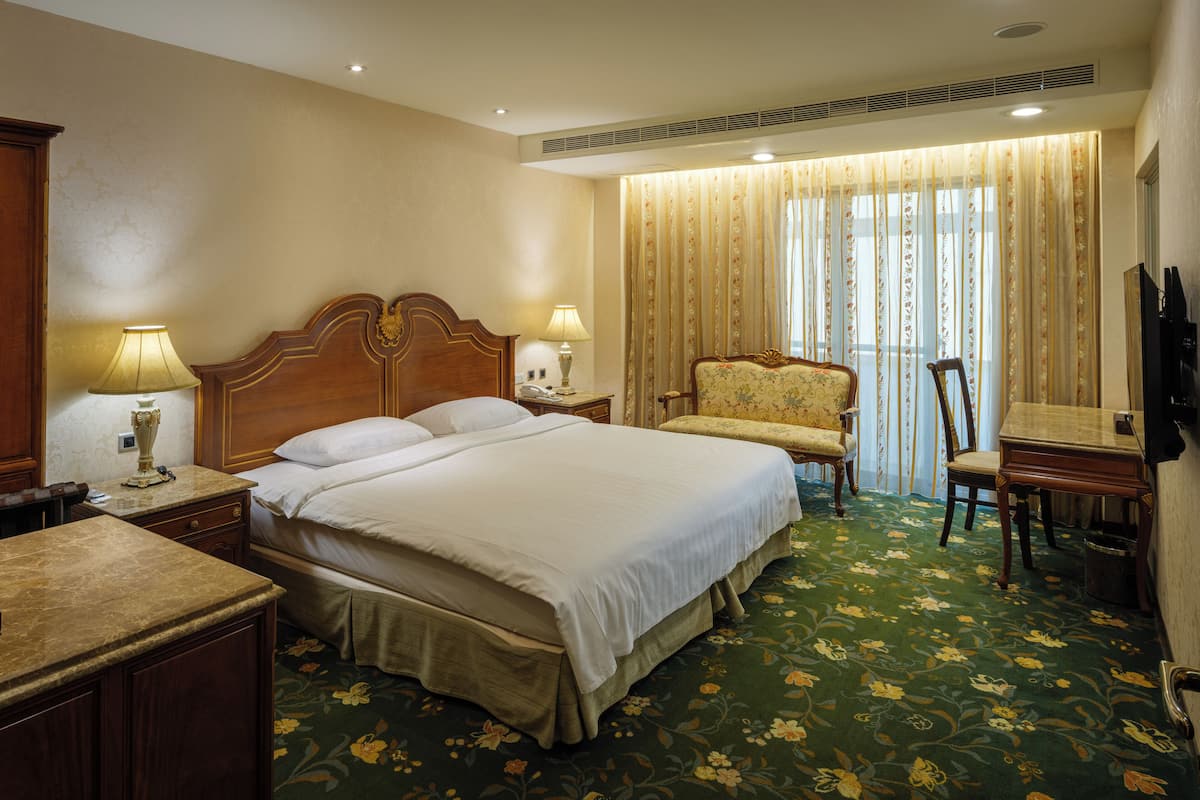 A hotel room with a large bed, two bedside tables with lamps, a chair, a desk, and a television.