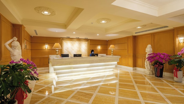 A hotel reception area with a marble counter, wooden paneling, and decorative statues. - Grand Pleasure Spring Hotel (Taipei)