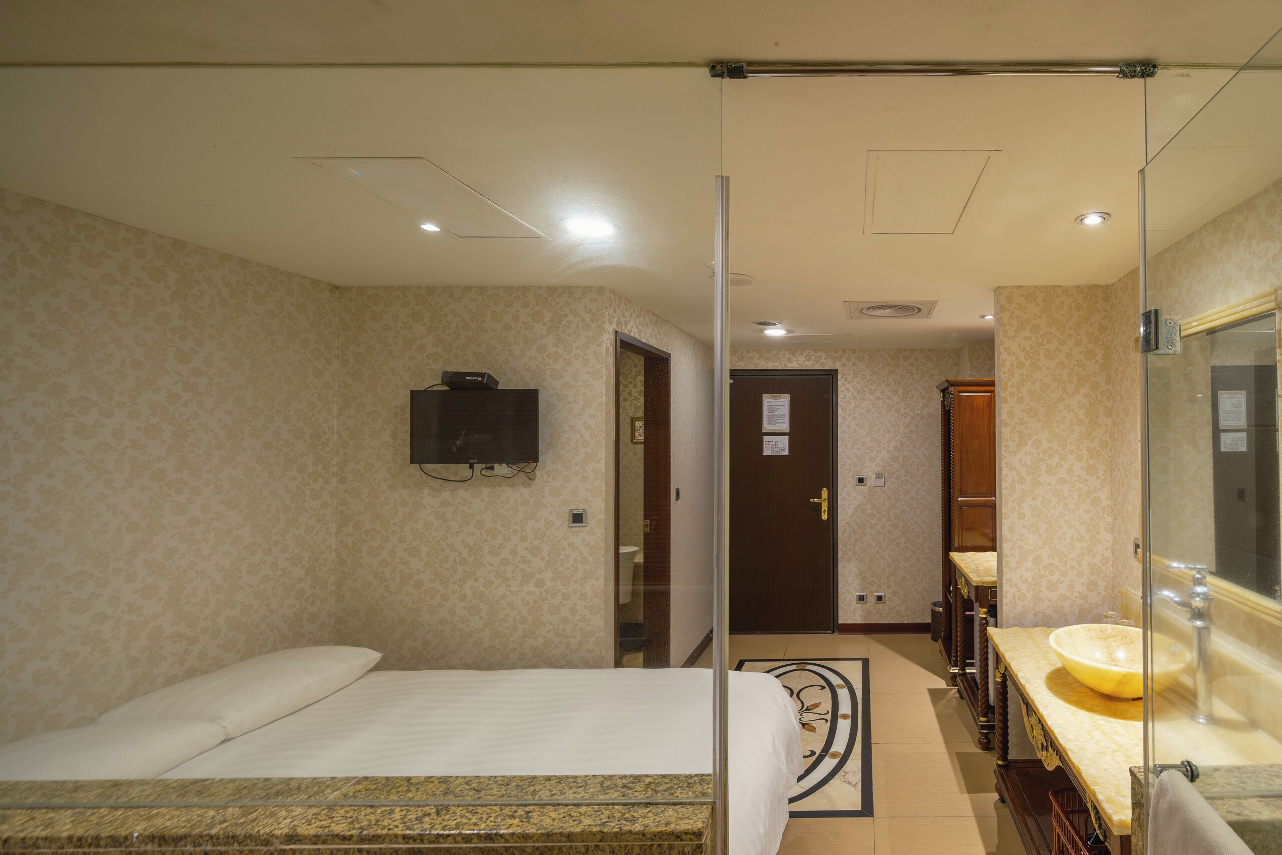 A hotel room with a bed, a bathroom with a sink and mirror, and a television on the wall.
