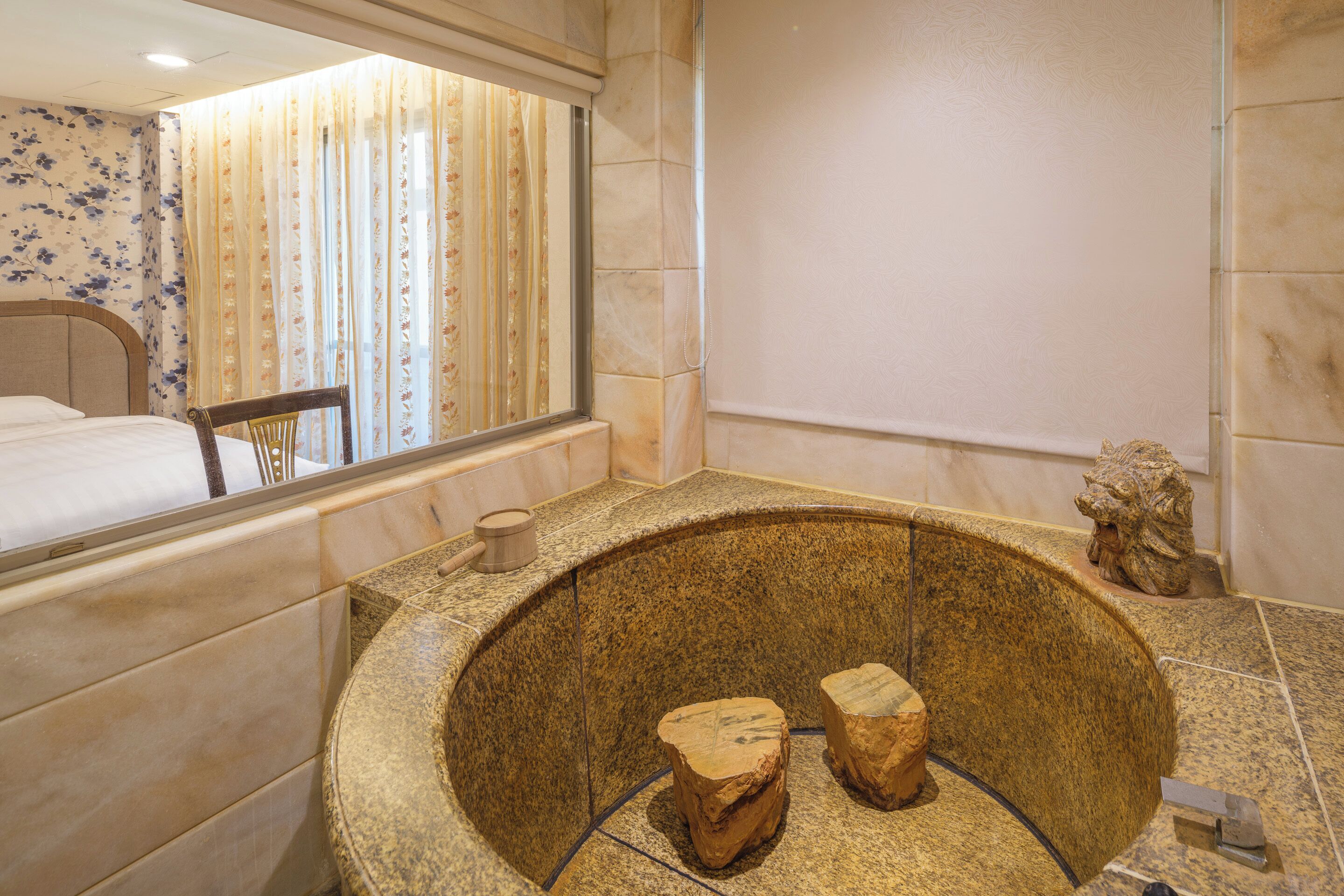 A bathroom with a stone sink, a mirror, and a bed visible through the window.
