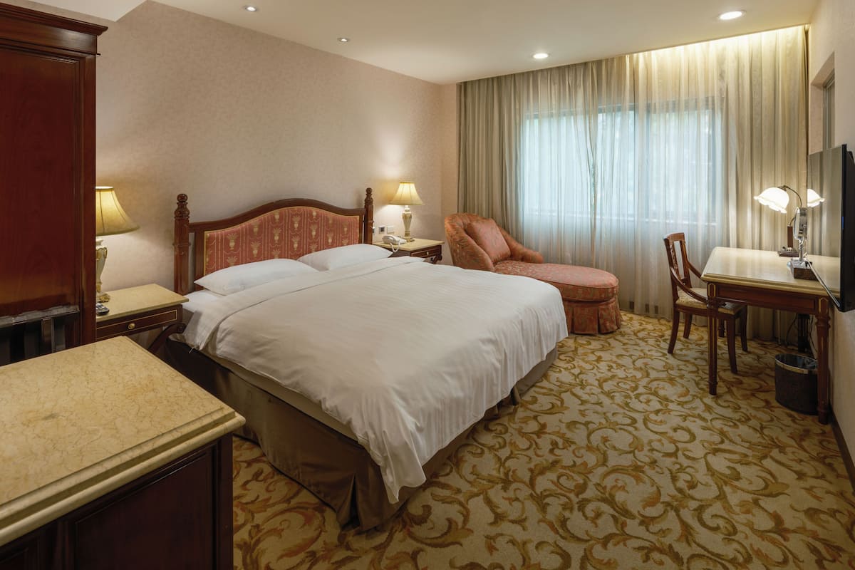 A hotel room with a large bed, two bedside tables with lamps, a desk with a chair, and a television.