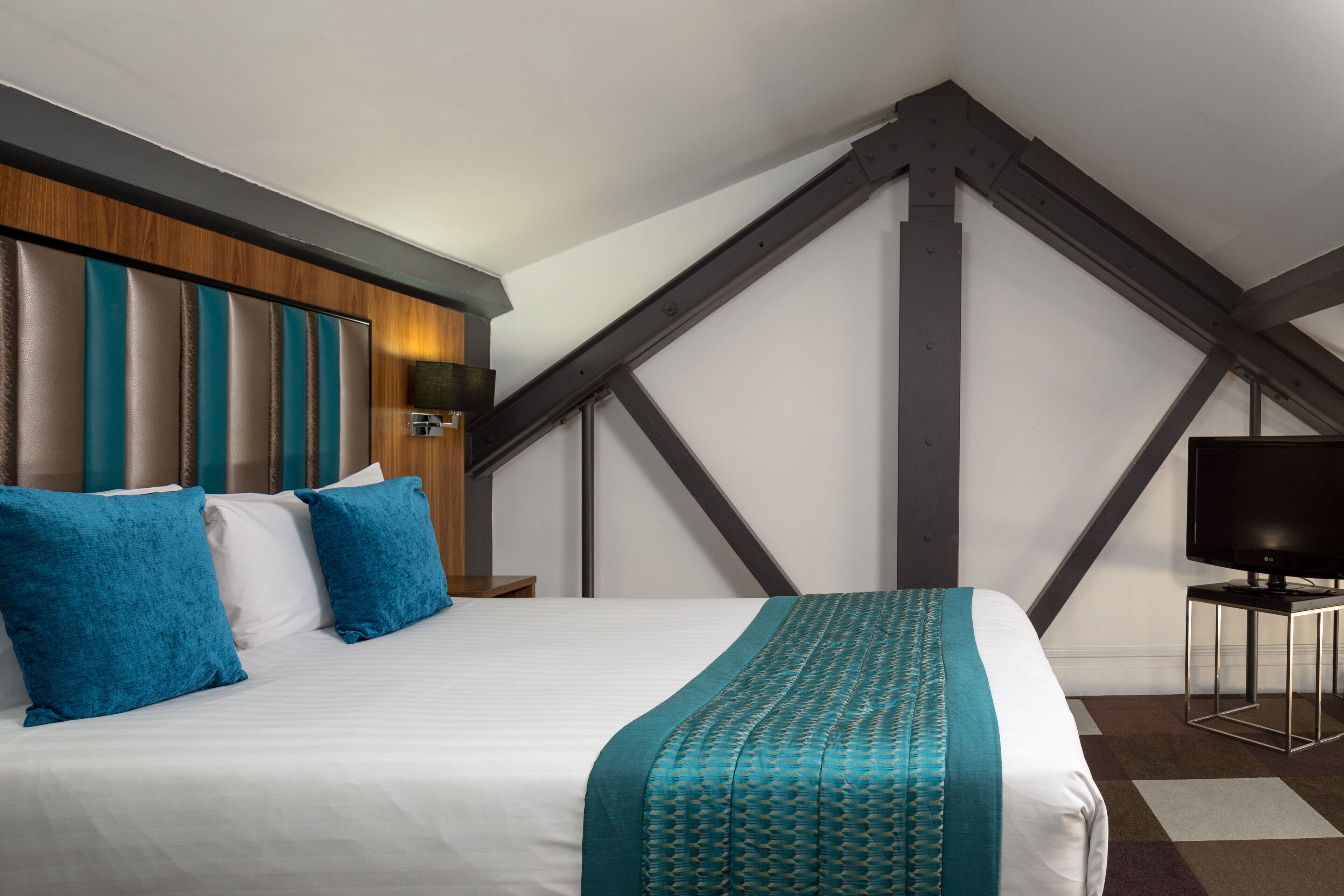 A hotel room with a large bed, a wooden headboard, and a television on a stand.