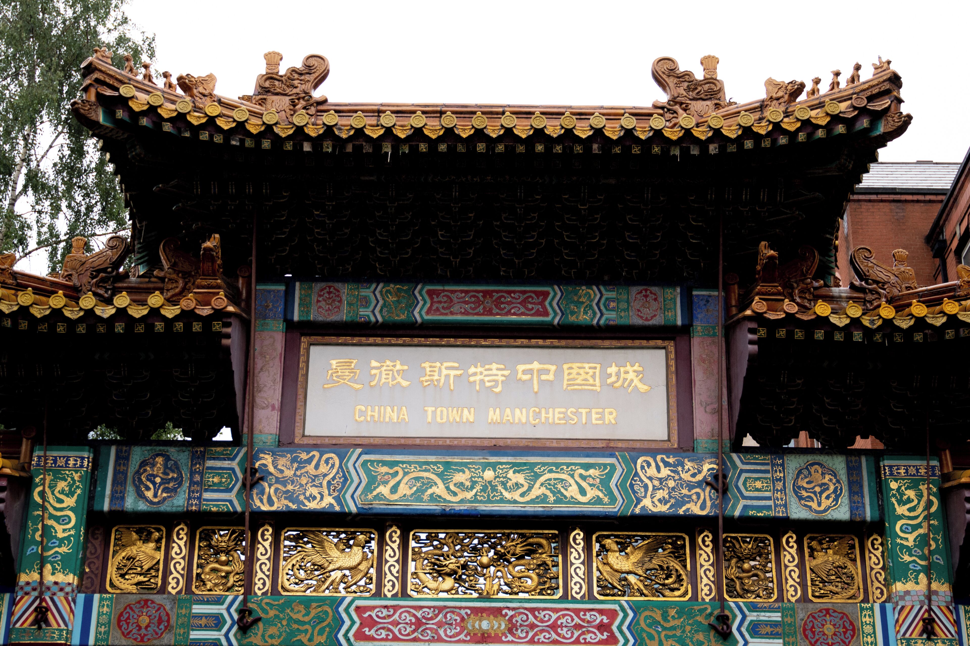 Een traditionele Chinese architectuurconstructie met versierde details en een bordje met de tekst 'China Town Manchester'.