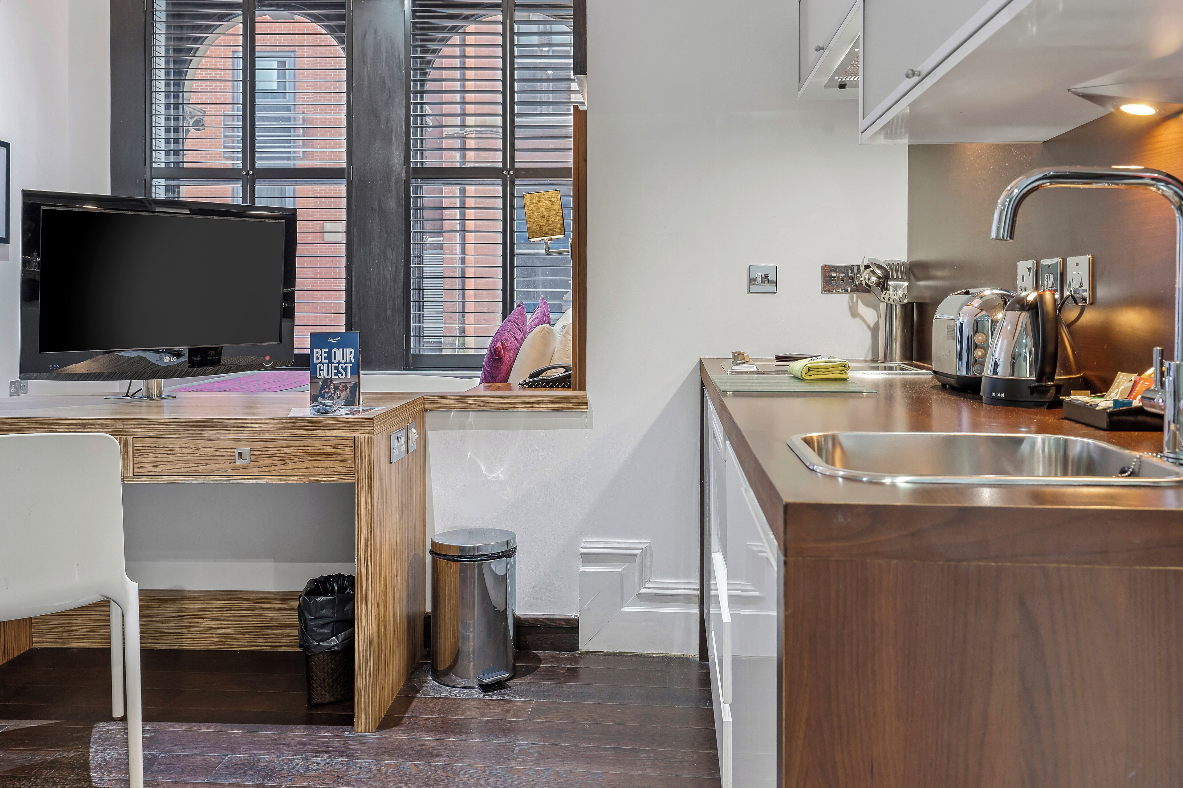Una cucina moderna con TV integrata, mobili in legno, lavello in acciaio inossidabile e una finestra con persiane.