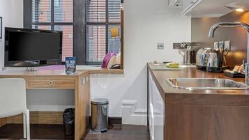 A modern kitchen with a built-in TV, wooden cabinetry, a stainless steel sink, and a window with blinds.