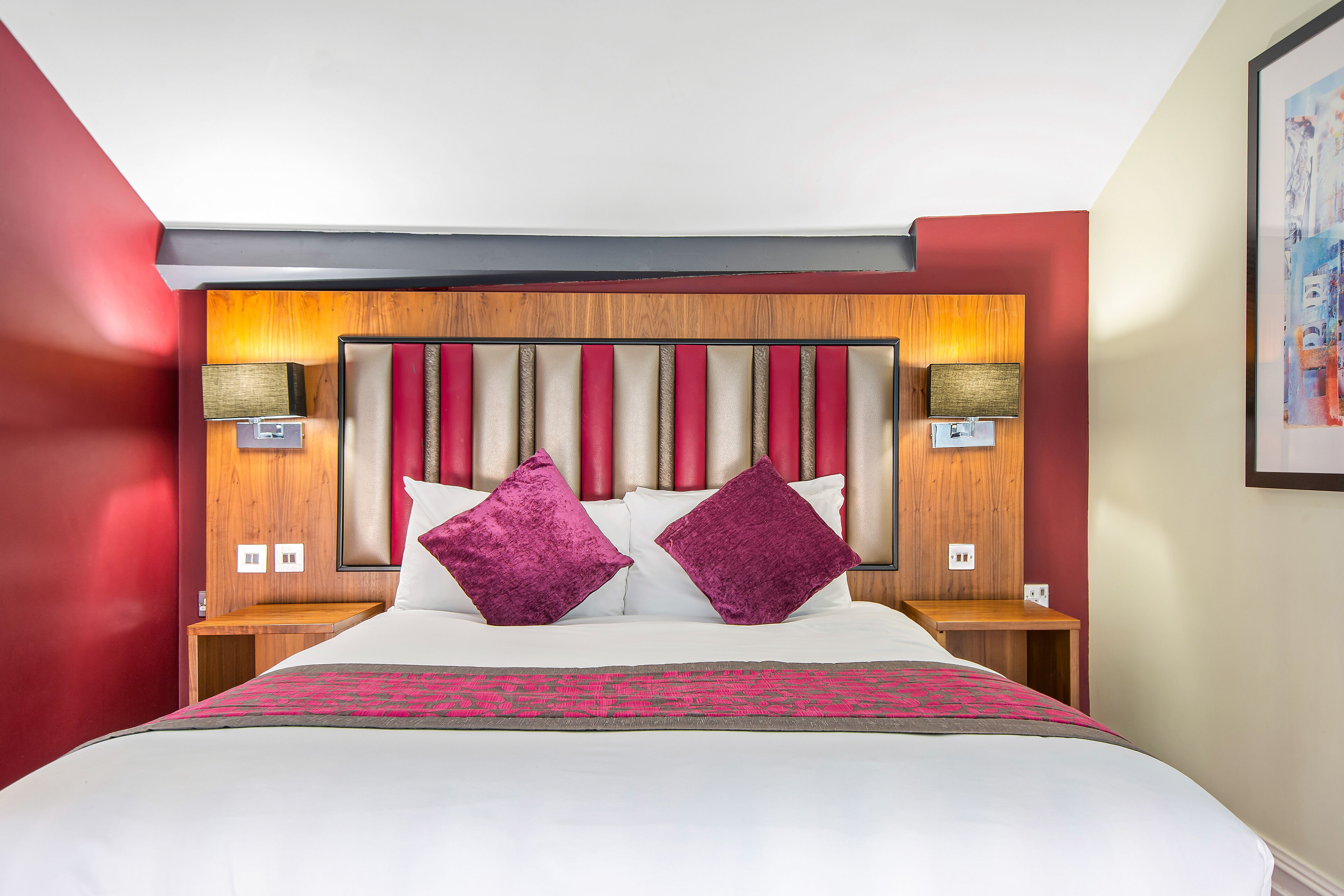 A hotel room with a large bed, red walls, a wooden headboard, and two bedside lamps.