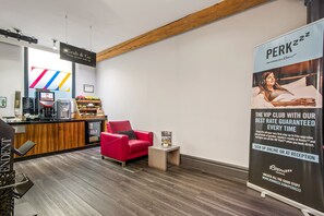 A modern hotel lobby with a reception desk, a red armchair, and a large poster advertising a VIP club. - Roomzzz Manchester City (Manchester)