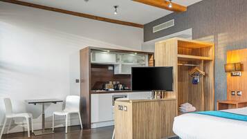 Et moderne hotelværelse med skrivebord i træ, fladskærms-tv, seng med blå detaljer og indbygget garderobeskab.