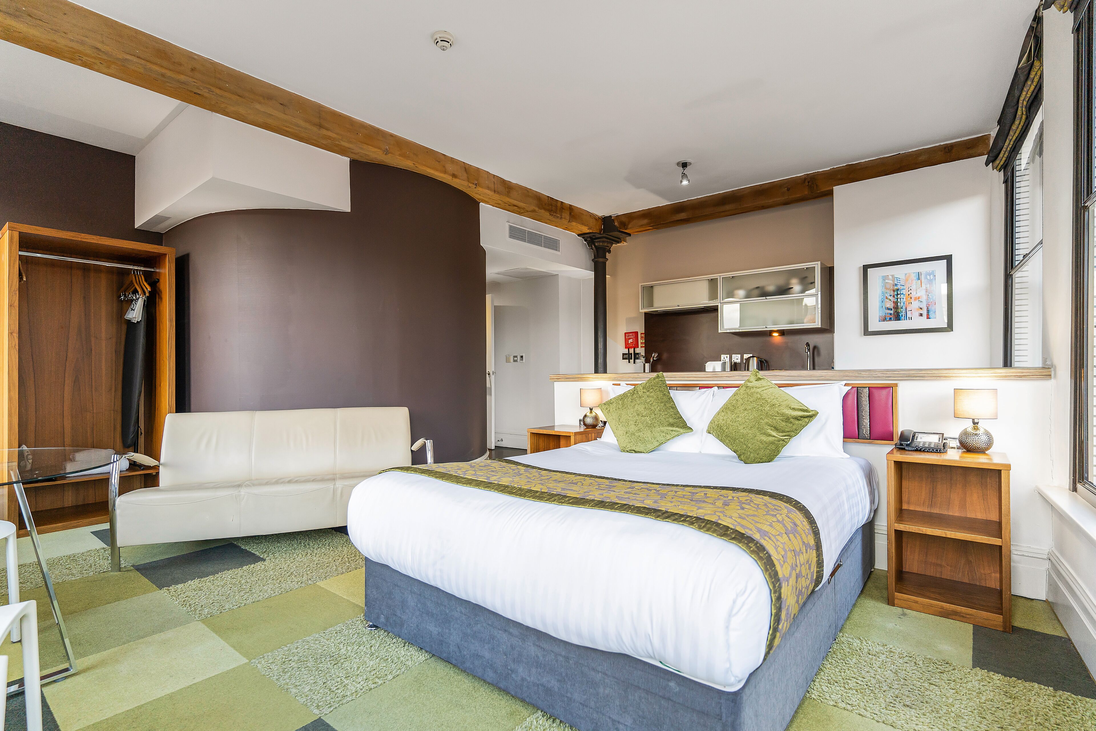 A bedroom with a bed, a sofa, a wooden nightstand, a lamp, and a mirror.