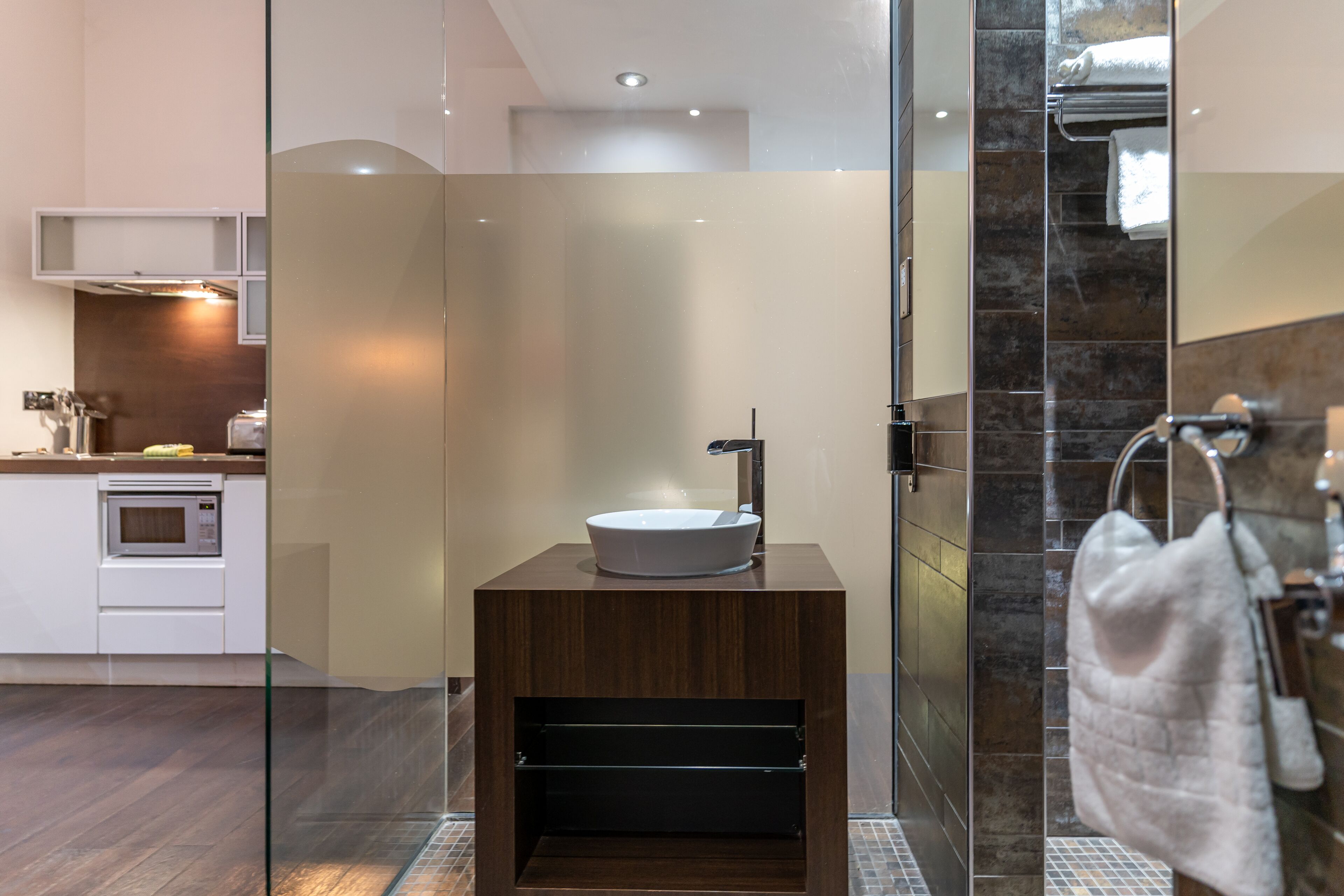 A modern bathroom with a glass-enclosed shower, a wooden vanity with a sink, and a towel rack.