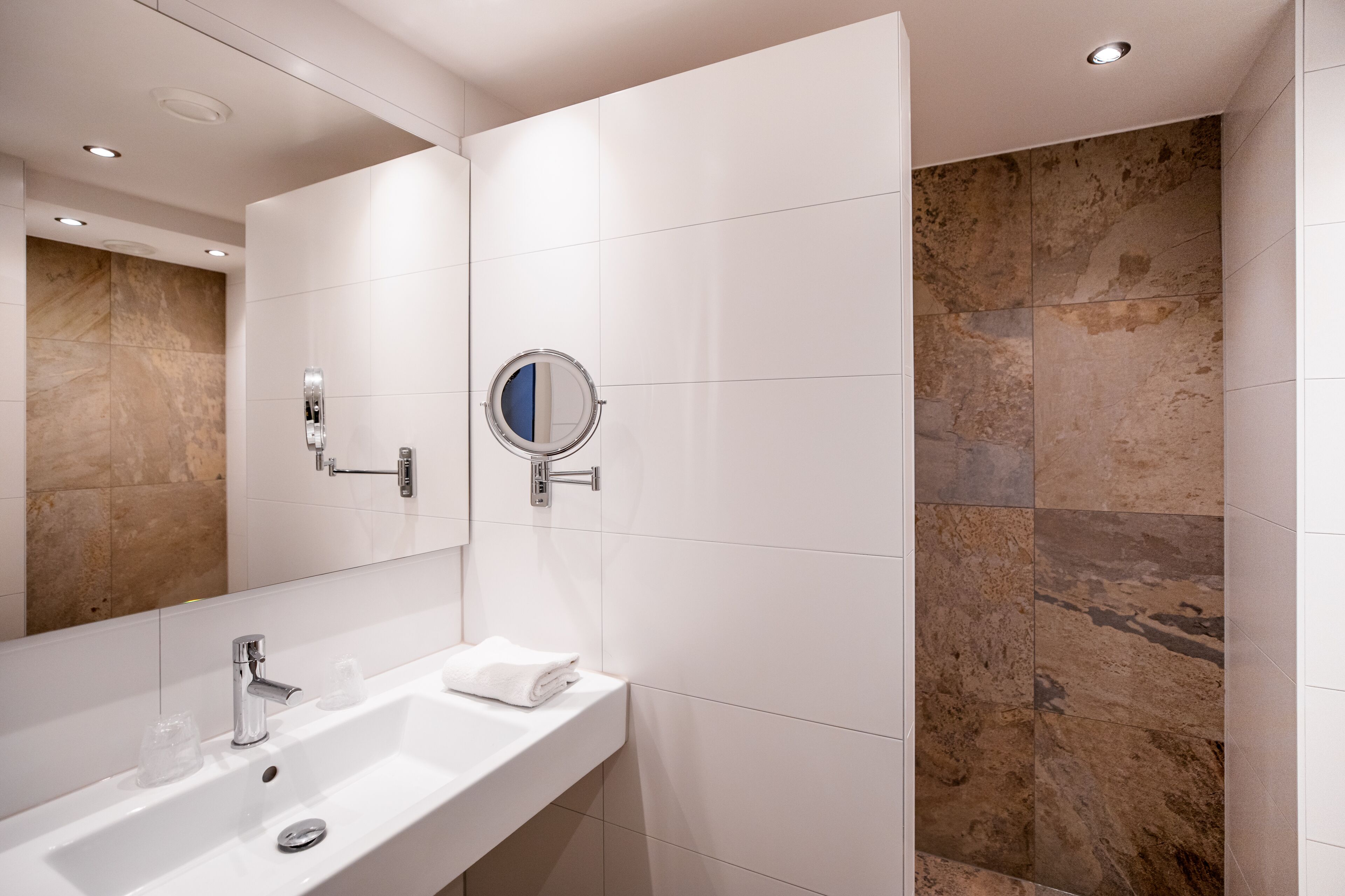 A modern bathroom with a white sink, mirror, and a shower area with beige tiles.