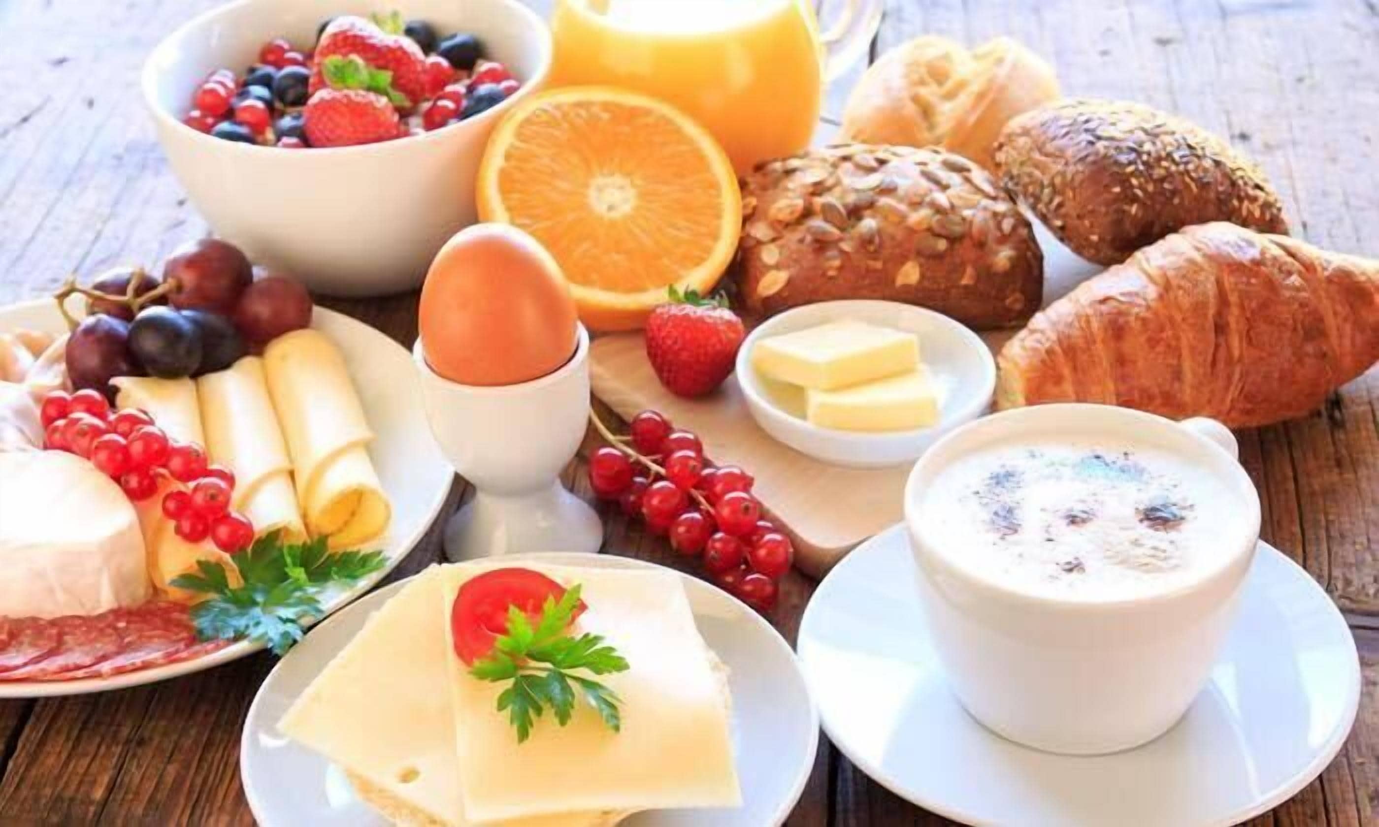 Une table mise pour le petit-déjeuner, avec divers aliments, notamment du pain, des fruits, du fromage et une tasse de café.