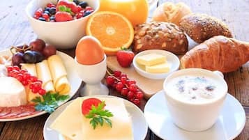 Une table mise pour le petit-déjeuner, avec divers aliments, notamment du pain, des fruits, du fromage et une tasse de café.