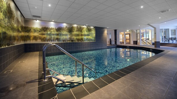 An indoor swimming pool with a glass wall, tiled flooring, and a staircase leading into the pool. - Boshotel Vlodrop (Vlodrop)