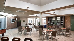 A spacious indoor area with multiple tables and chairs, a pool table, and a brick wall with a clock. - Boshotel Vlodrop (Vlodrop)