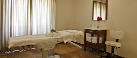 A medical examination room with a bed, examination table, and a chair.