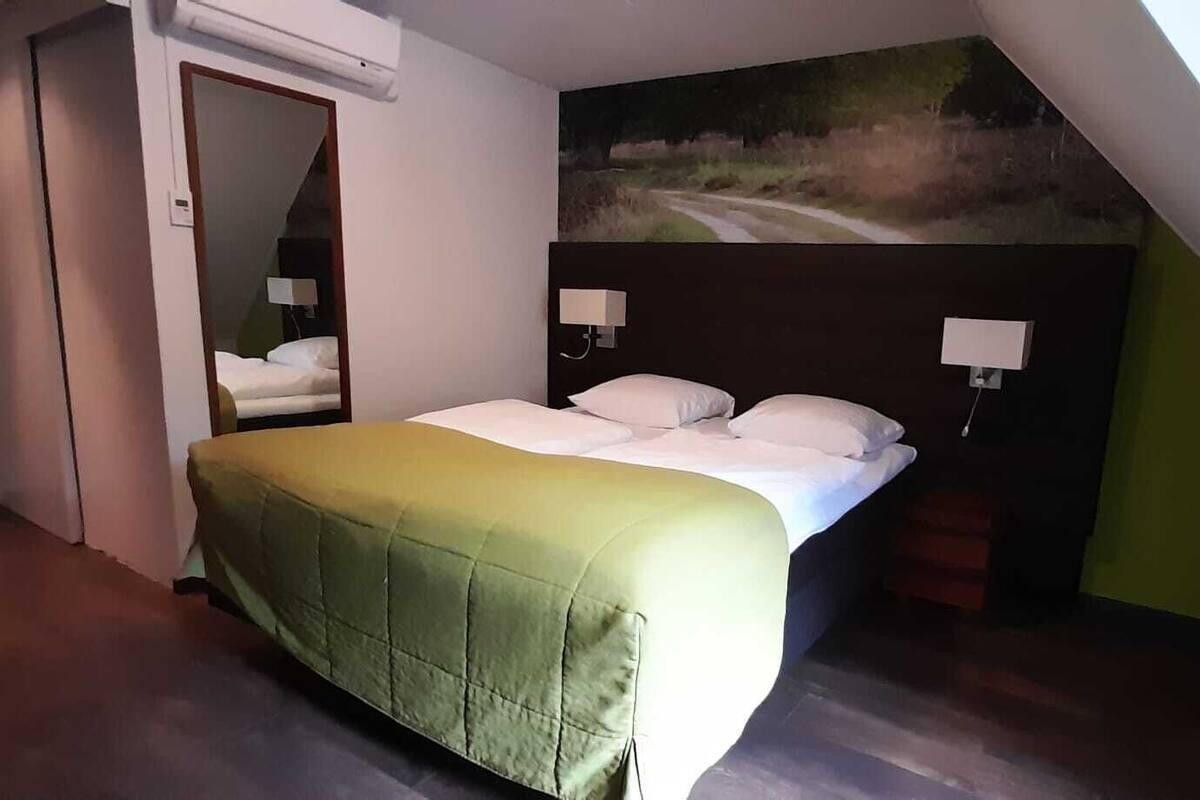 A hotel room with a bed, a painting on the wall, and a door.
