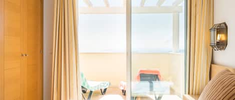 A hotel room with a bed, a wooden wardrobe, a balcony with a table and chairs, and a view of the outside.