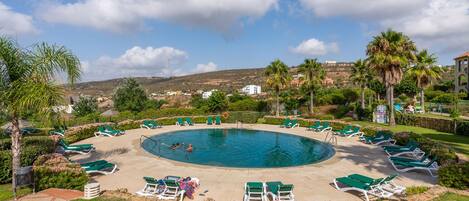 A pool area with sun loungers and a view of the surrounding landscape.