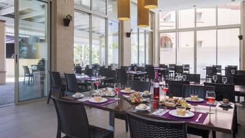 Un restaurante espacioso con varias mesas y sillas, ventanas amplias y lámparas colgantes.