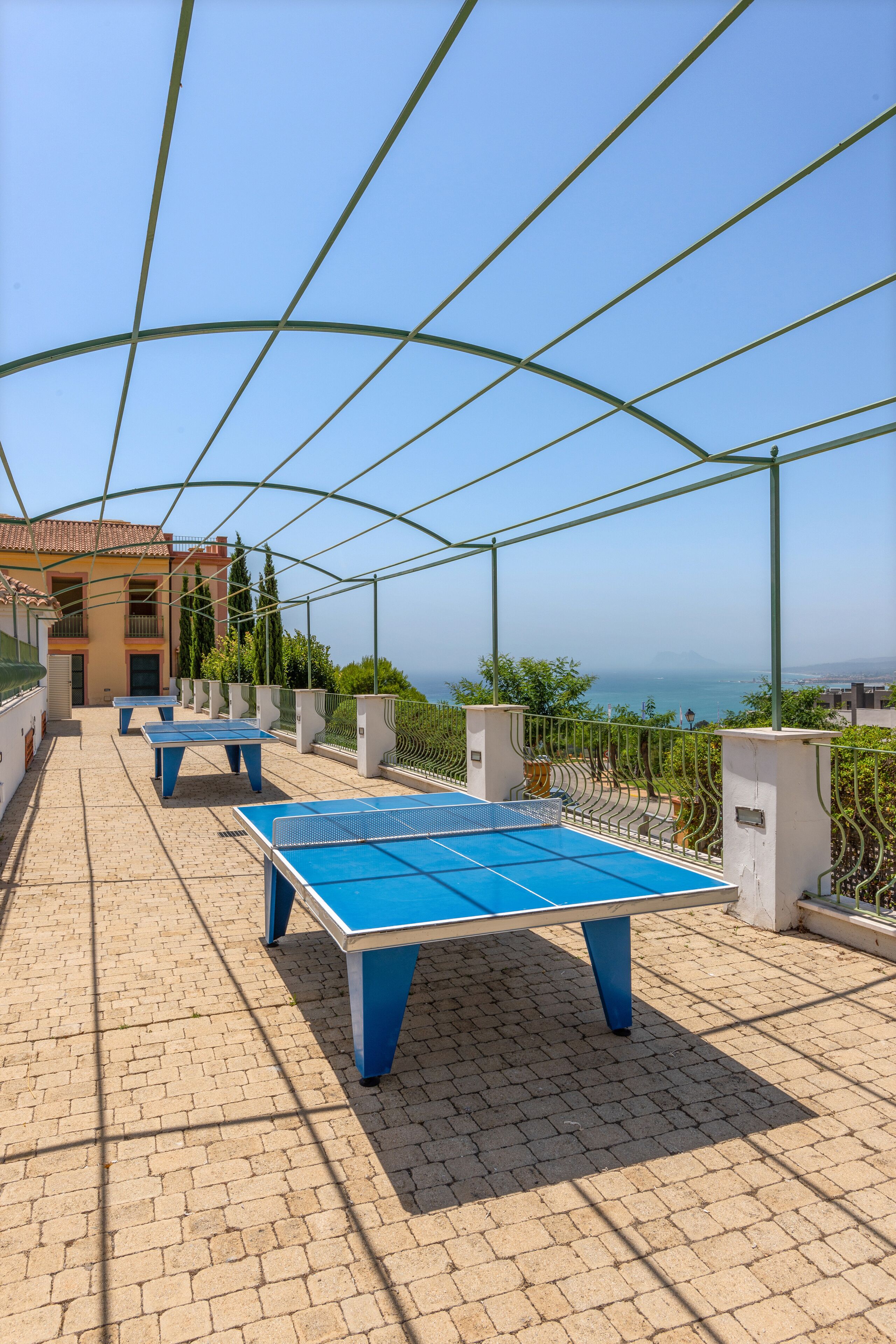 An outdoor area with ping pong tables, a covered seating area, and a view of the sea.