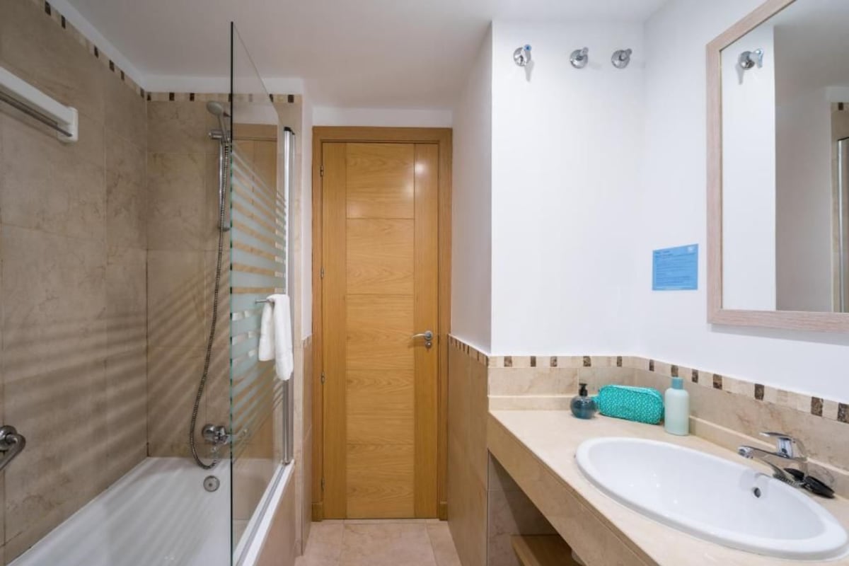 A bathroom with a glass-enclosed shower, a wooden door, a white sink, and a mirror above it.