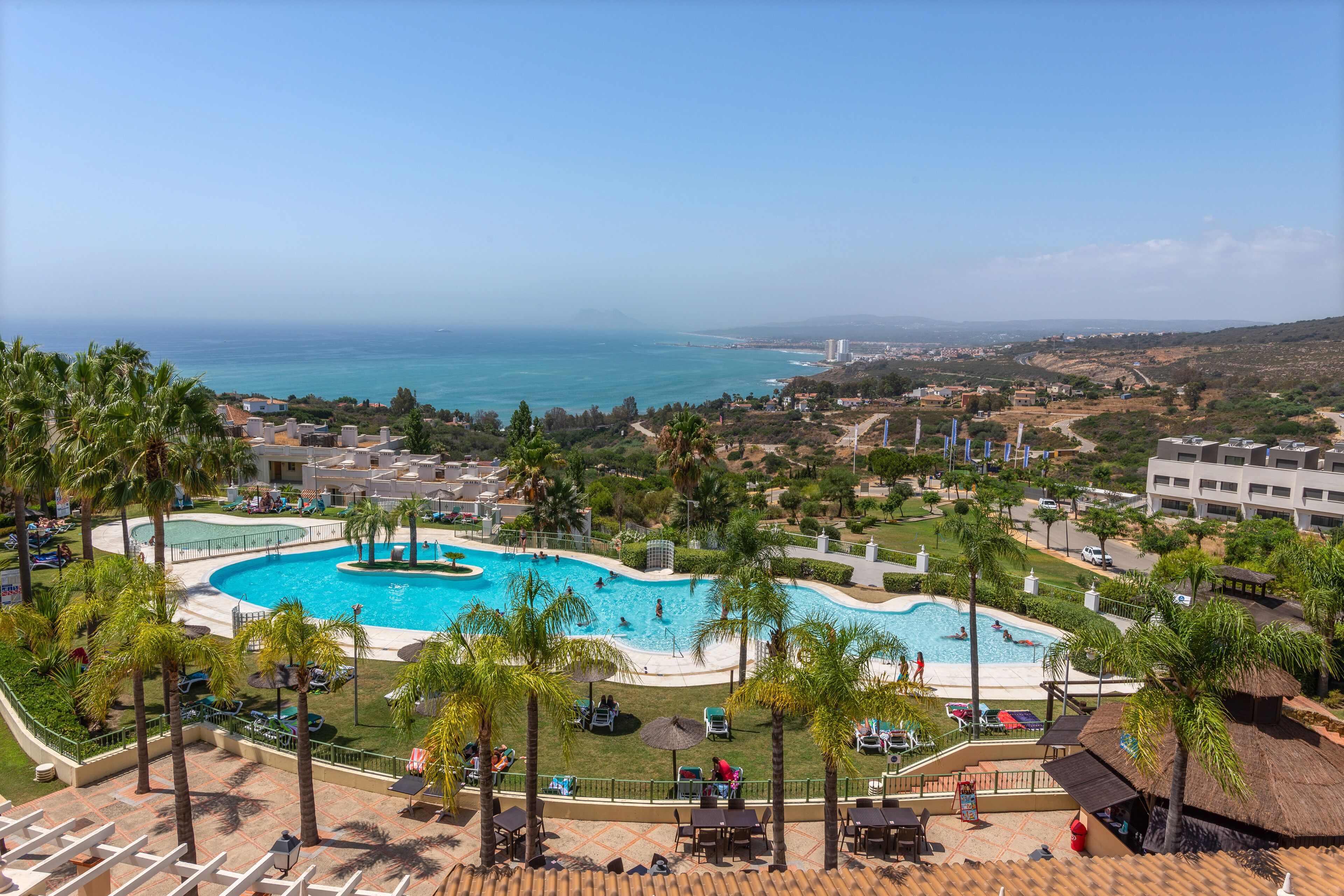 Een resort met een groot zwembad, omgeven door palmbomen, een strand en uitzicht op de oceaan.
