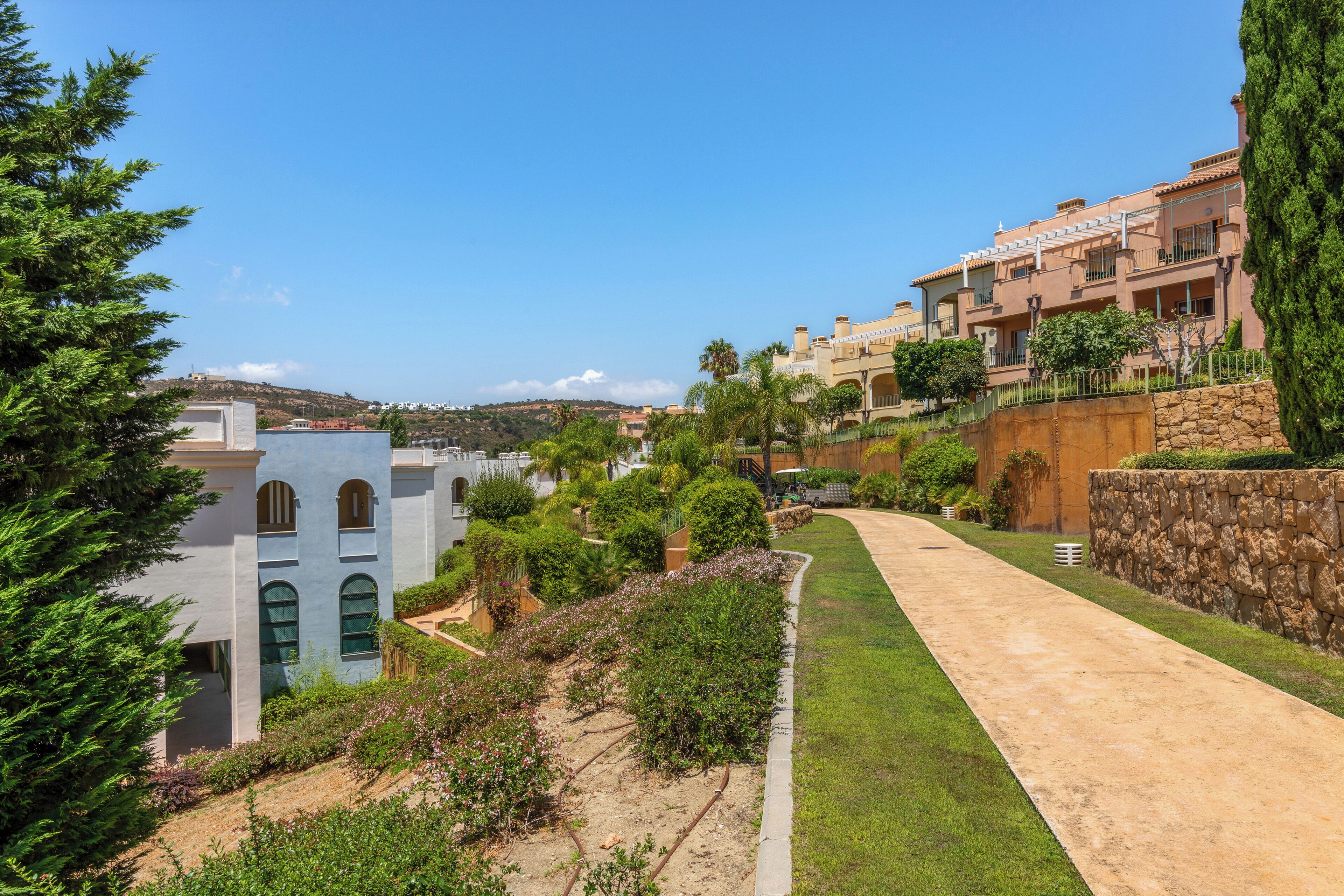 Zona residencial con un sendero pavimentado, muros de piedra y abundante vegetación.