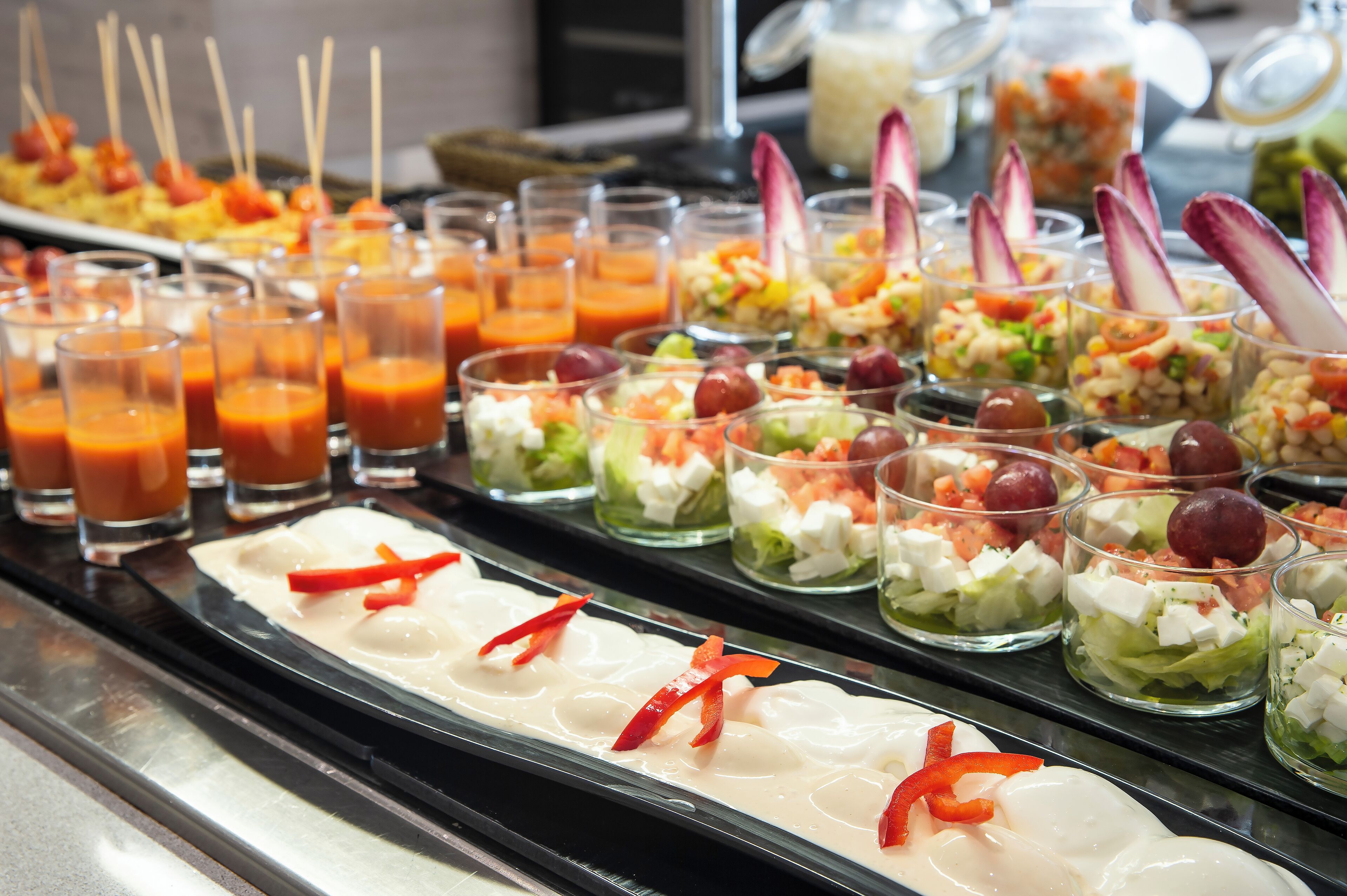 A buffet with various food items including salads, dips, and juices.