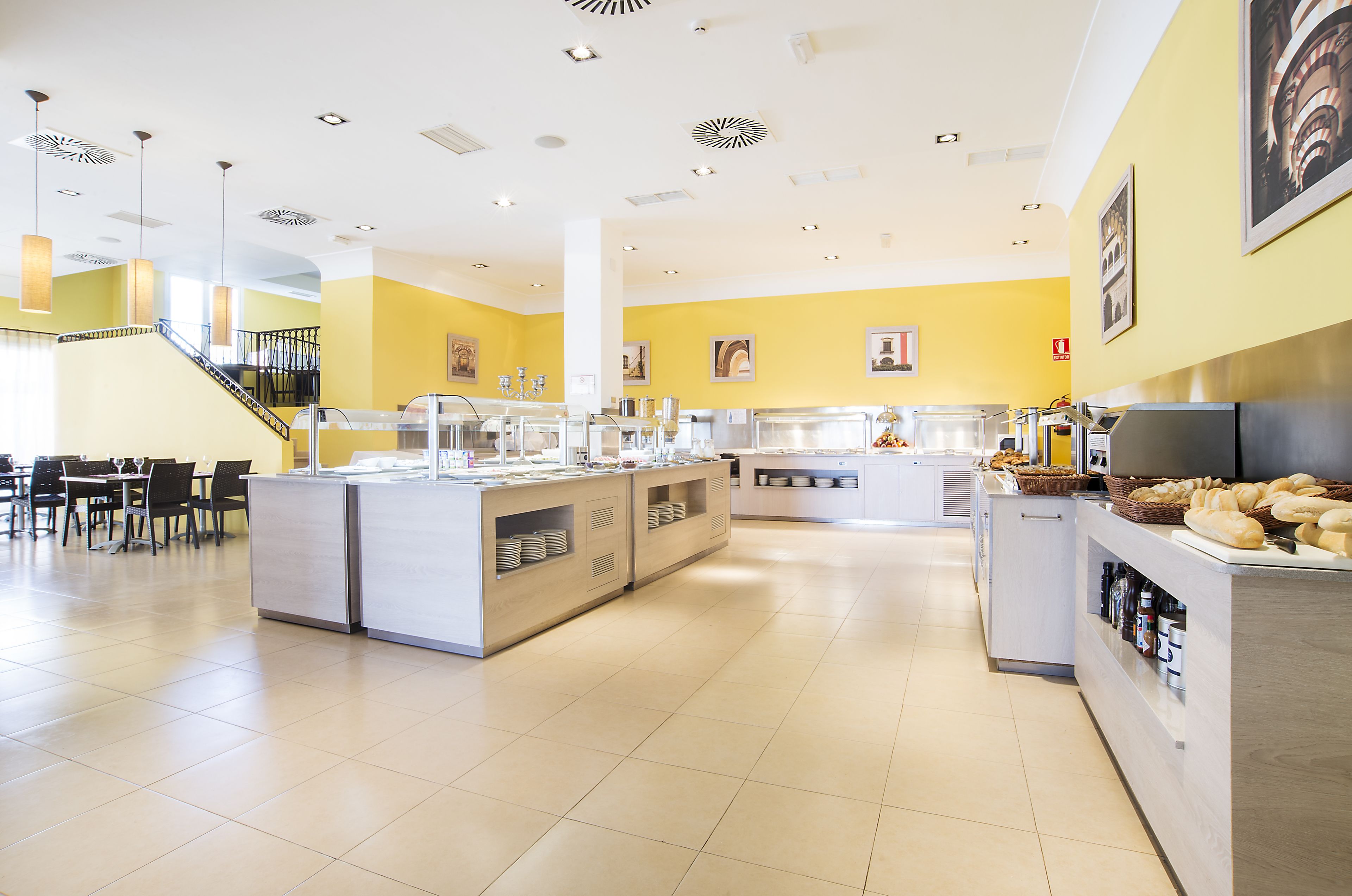 A bright, spacious kitchen area with multiple counters, a dining area with tables and chairs, and a staircase leading to an upper level.