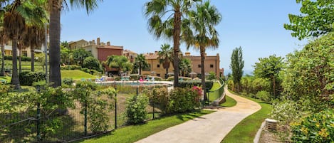 Un sendero que lleva a una zona de piscina con palmeras y un edificio al fondo.
