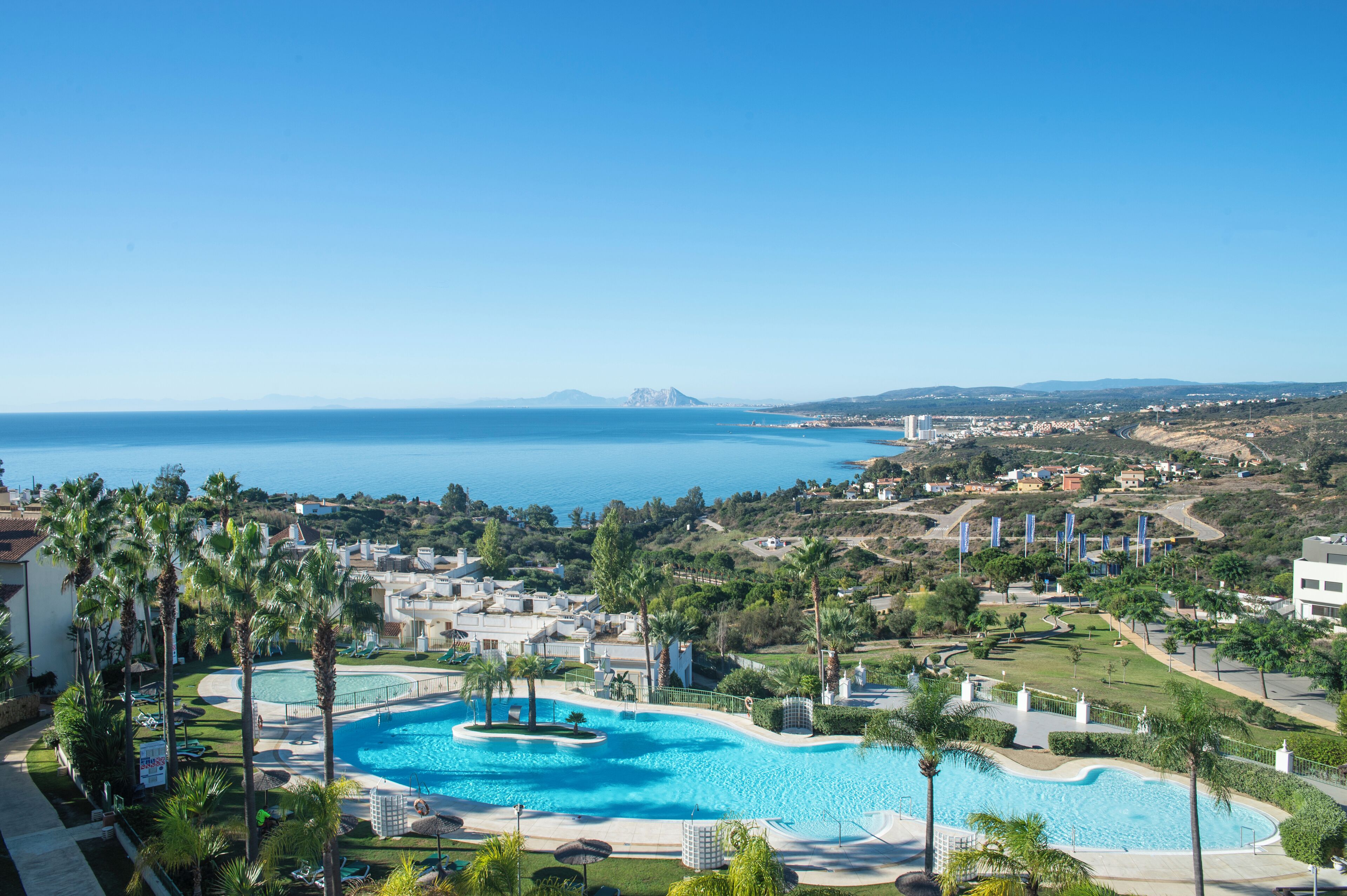 A resort with a large swimming pool surrounded by palm trees and a view of the sea.