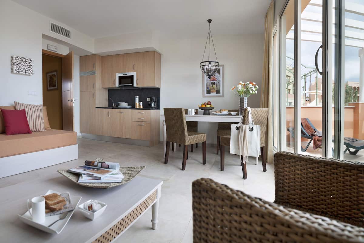 A modern living room with a sofa, dining table, wicker chairs, and a kitchen in the background.