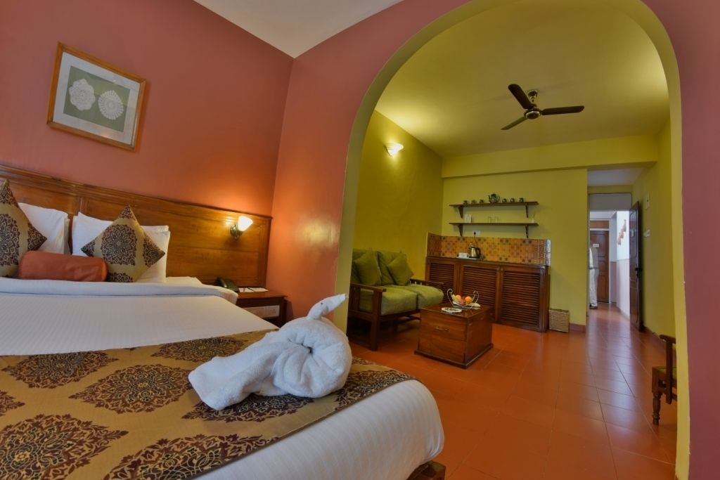 Una habitación de hotel con una cama, un sillón verde, un armario de madera y un ventilador de techo.