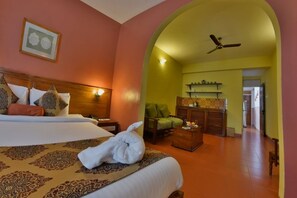 A hotel room with a bed, a green armchair, a wooden cabinet, and a ceiling fan. - Pride Sun Village Resort & Spa (Arpora)