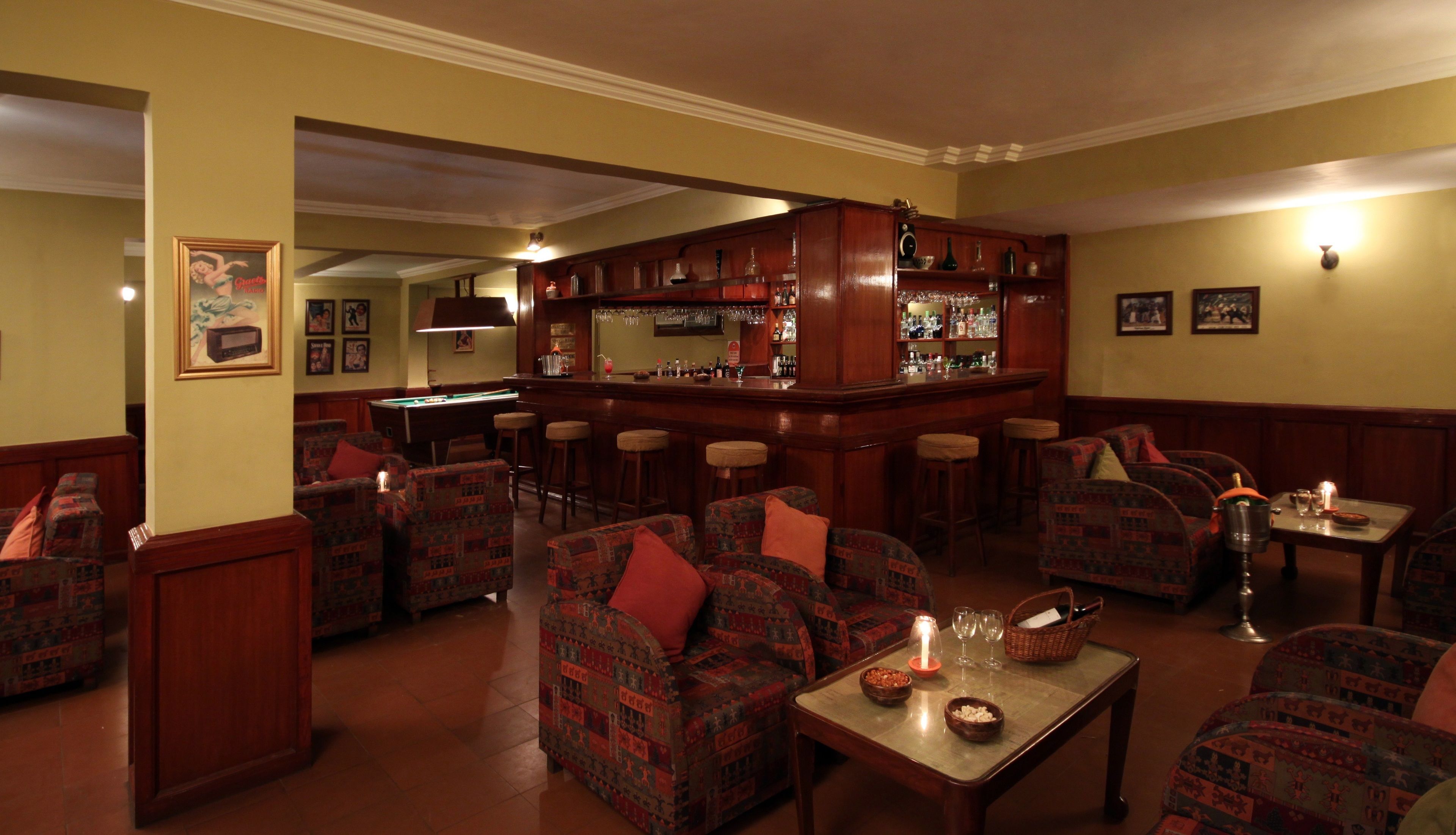 A bar area with multiple stools, a pool table, and a bar counter with various bottles and glasses.