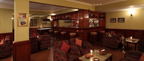 A bar area with multiple stools, a pool table, and a bar counter with various bottles and glasses.